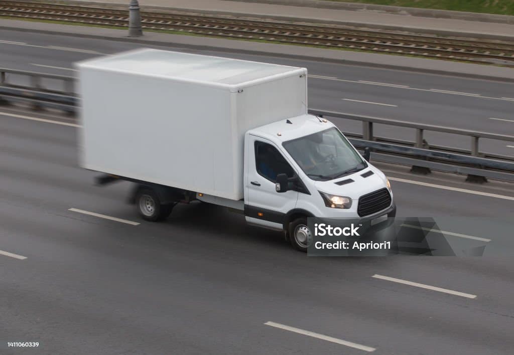 A white box truck speeding along a multi-lane highway with visible motion blur.